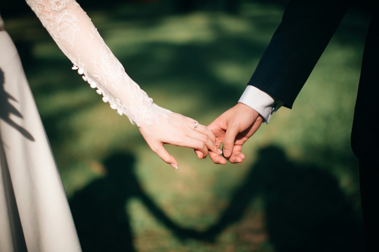 Bride and groom holding hands, shadows on the grass