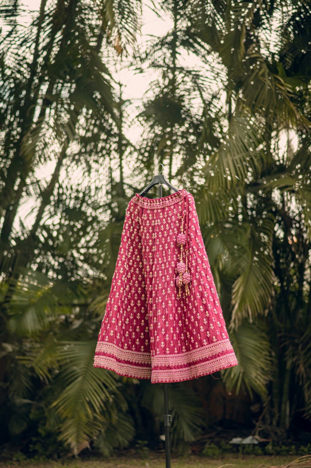 Bridal lehenga hanging beneath palm leaves before the ceremony